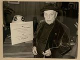 photographie en noir et blanc d'un homme portant un chapeau et un manteau, tenant une pancarte