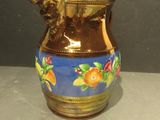 a brown and blue vase with oranges on it on a table