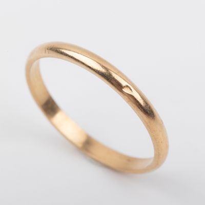 a gold wedding ring with a thin band on a white background