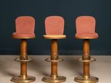 three wooden stools with pink upholstered chairs in front of a blue wall