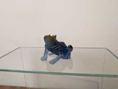 une petite figurine représentant une grenouille assise sur une table en verre