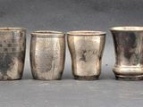 six silver shot glasses lined up in a row on a gray surface