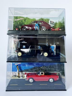 trois petites voitures dans une vitrine posée sur une surface blanche