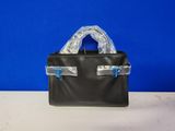 un sac à main en cuir noir muni de poignées en plastique transparent, posé sur une table blanche