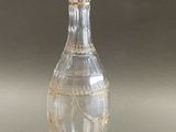 a clear glass bottle with a gold decoration on it