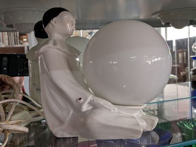 une statue représentant une femme tenant une balle, posée sur une étagère en verre