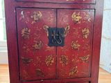 an old red cabinet with gold flowers on it sitting on a hard wood floor