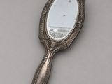 an antique silver mirror with a handle on a gray surface