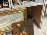 un tableau posé par terre, à côté d'un tableau posé sur une étagère