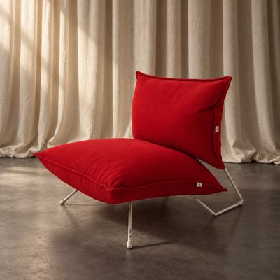une chaise rouge sur laquelle est posé un coussin rouge, devant un rideau blanc