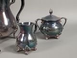 three silver teapots and two silver cups on a table