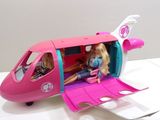 une poupée Barbie assise dans un petit avion rose avec deux petites filles à l'intérieur