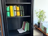 une bibliothèque noire sur laquelle sont posés de nombreux livres, dans une pièce