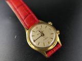 a gold watch with a red strap on a black surface