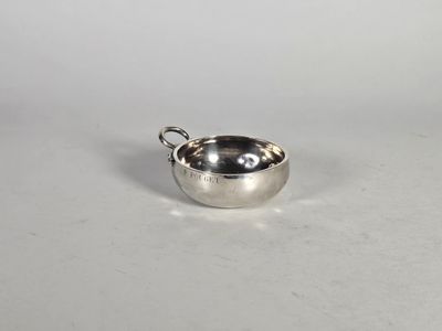un petit bol en argent avec une poignée sur une surface blanche