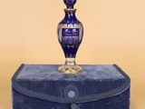 une image représentant un flacon de parfum en verre bleu posé sur une boîte bleue