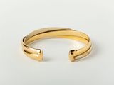 a gold cuff bracelet with a curved design on a white background