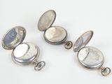 three small silver pocket watches are sitting on a white surface