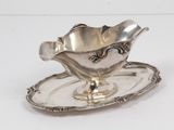 une assiette en argent posée sur une soucoupe, le tout sur une surface blanche