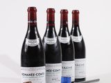 quatre bouteilles de vin et un maillet en bois posés sur une surface blanche