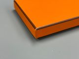 une boîte orange posée sur une table grise, à côté d'une paire de ciseaux
