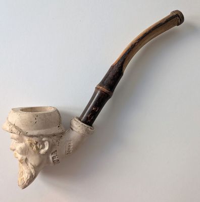 une pipe surmontée d'une tête d'homme coiffée d'un chapeau
