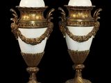 une paire de vases blancs et dorés posés sur des socles en marbre, sur fond noir