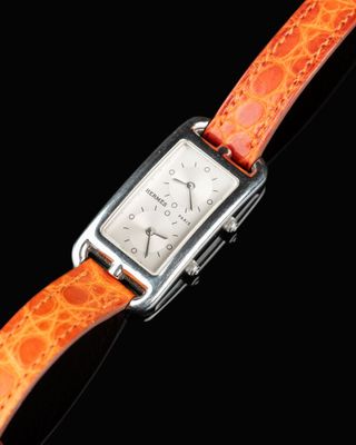 an orange watch with a silver case on a black background