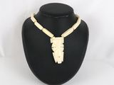 a white necklace with a carved face on a black mannequin
