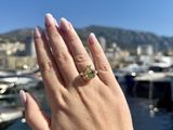 woman ' s hand holding up a yellow diamond ring in front of a marina