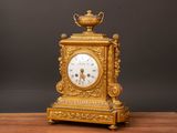 a gold clock sitting on a wooden table with a black background