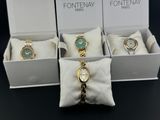 three watches in a white box with a gold chain and a green dial