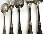 five spoons and a fork are lined up on a white surface