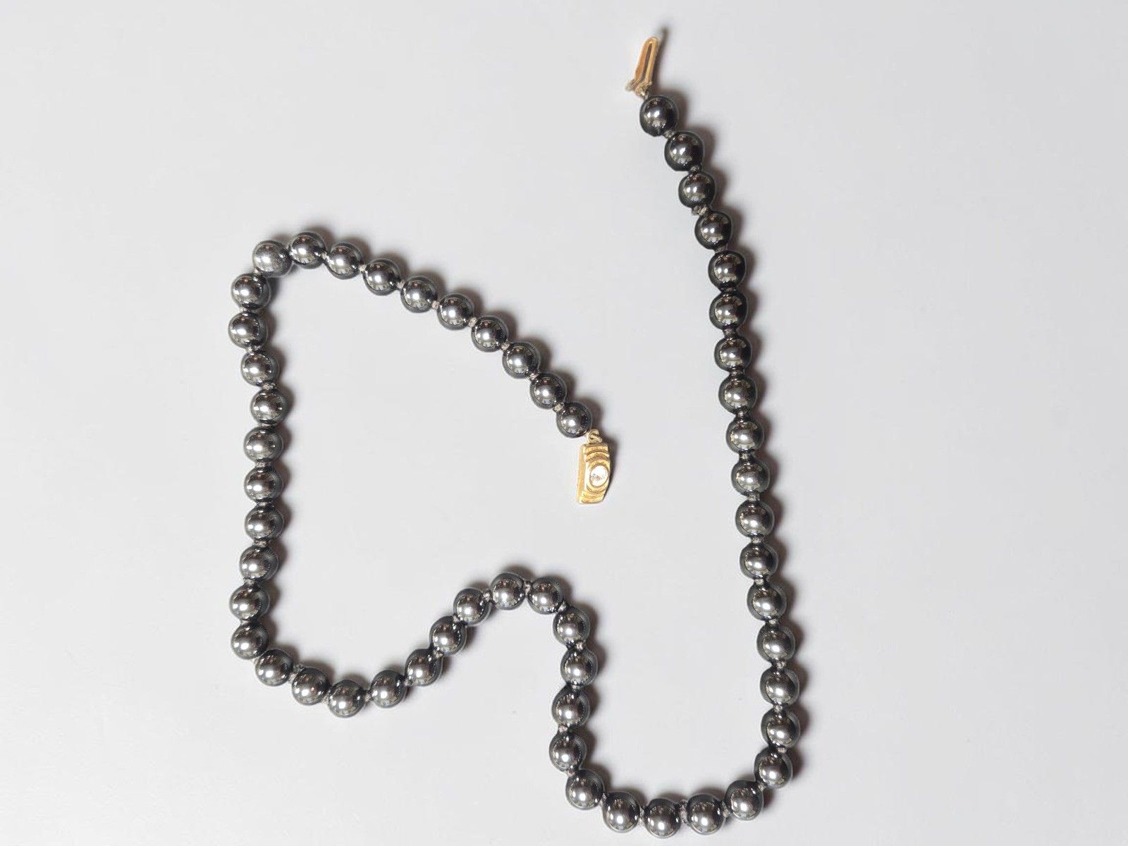 Collier de boulles d'hématite, fermoir en métal doré orné d'une pierre blanche d'imitation. Lg. 52cm