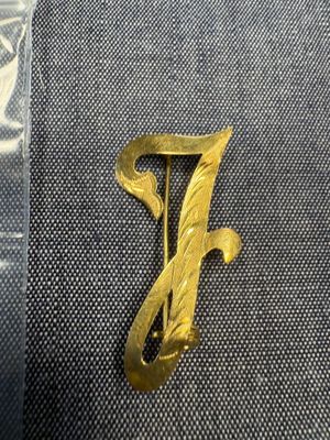 un gros plan sur une broche en or sur laquelle figure la lettre « f »