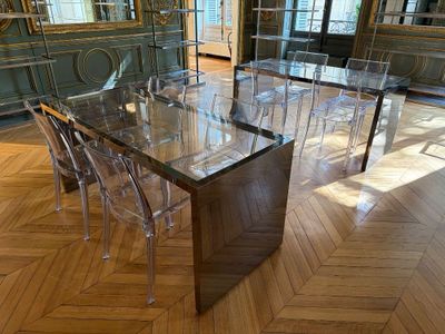 une table à manger en verre entourée de chaises transparentes, au milieu de la pièce