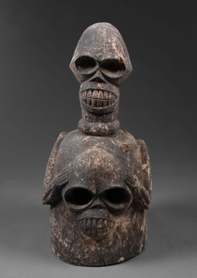 une vieille statue en bois surmontée de deux crânes