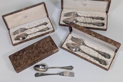 Plusieurs pièces d'argenterie sont disposées dans un coffret posé sur une surface blanche
