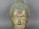 statue représentant une tête de Bouddha sur un socle noir, avec un fond gris