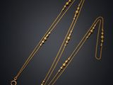 a gold necklace and a gold chain with beads on a black background