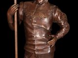 bronze statue of a man with a scythe standing next to a flag