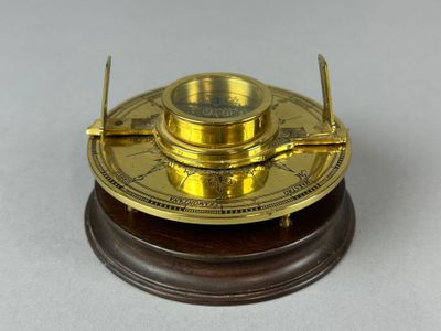 une horloge ancienne en laiton posée sur un socle en bois, elle-même posée sur une surface blanche