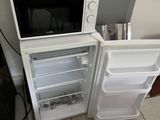a small white refrigerator with a microwave on top of it