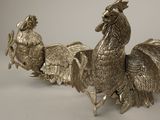 two silver colored roosters standing next to each other on a table