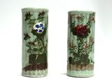 two green vases with flowers on them on a white surface