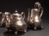 two silver teapots and a coffee pot sitting on a table