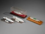 three miniature model boats and a wooden display case on a gray surface