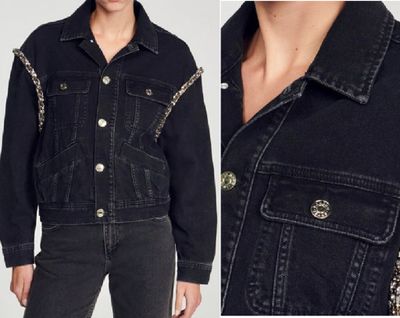 a woman wearing a black denim jacket with chains on the sleeves