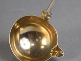 a gold spoon with a handle on a gray surface