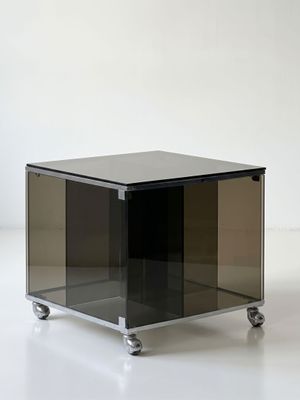 an image of a black glass table with wheels on a white surface